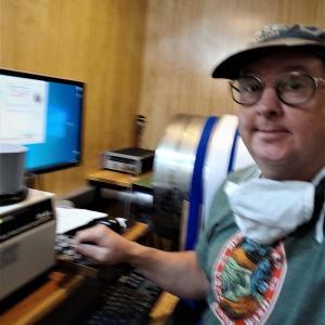 Bernie Housen at a computer wearing hat and t-shirt with face mask around neck