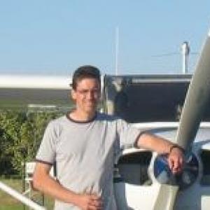 Brad Johnson wearing t-shirt standing by his small, single engine plane