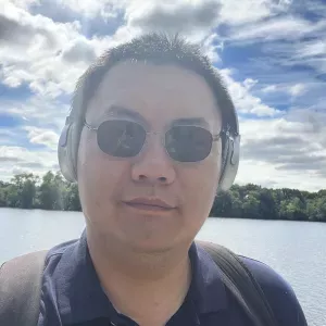 Photo of Peng Gao wearing sunglasses and headphones with body of water in background.